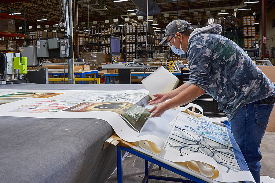 Worker collecting pieces of art off assembly line.